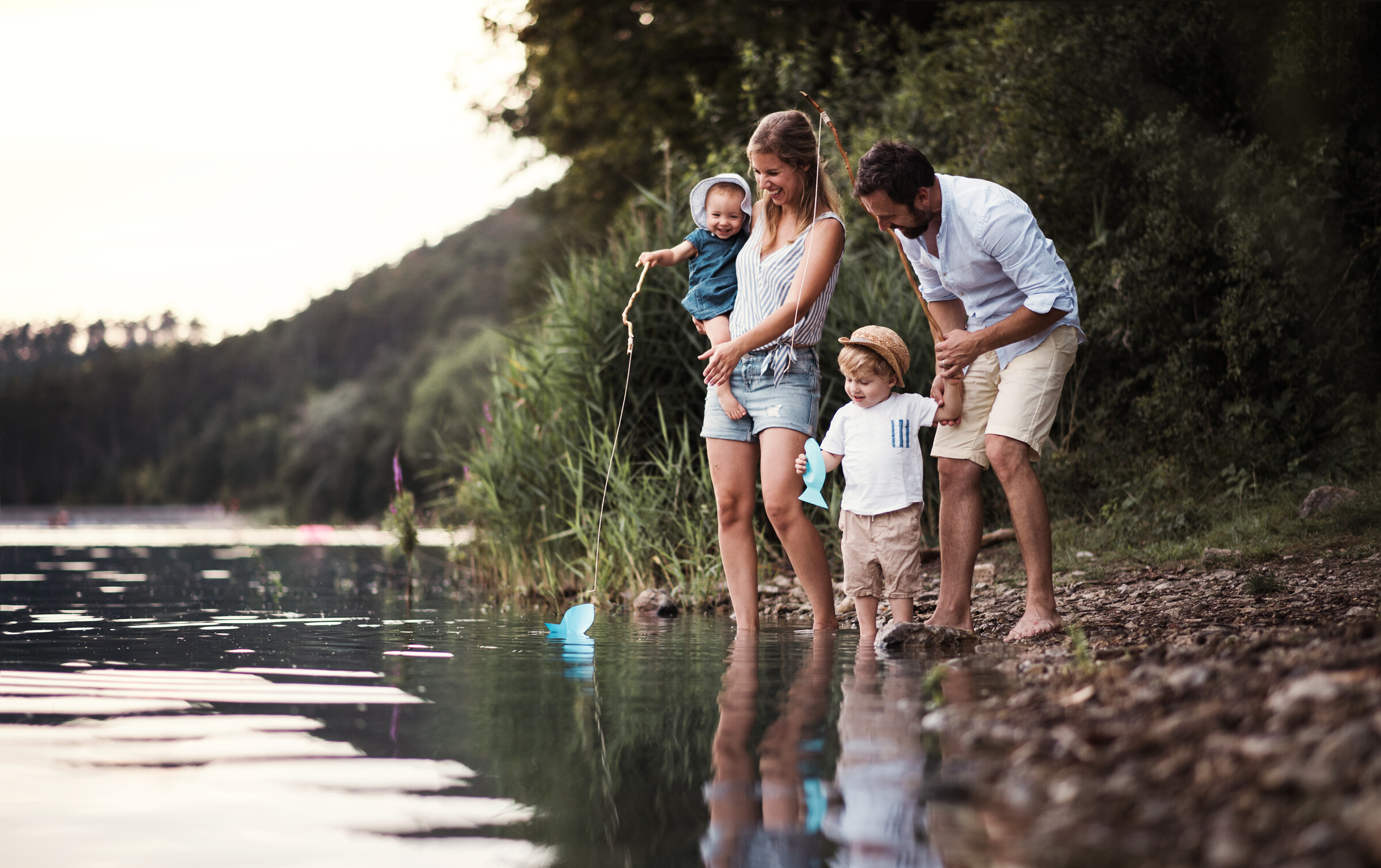 Eine junge Familie mit zwei kleinen Kindern stehen zusammen an einem Fluss an einem schönen Sommertag.