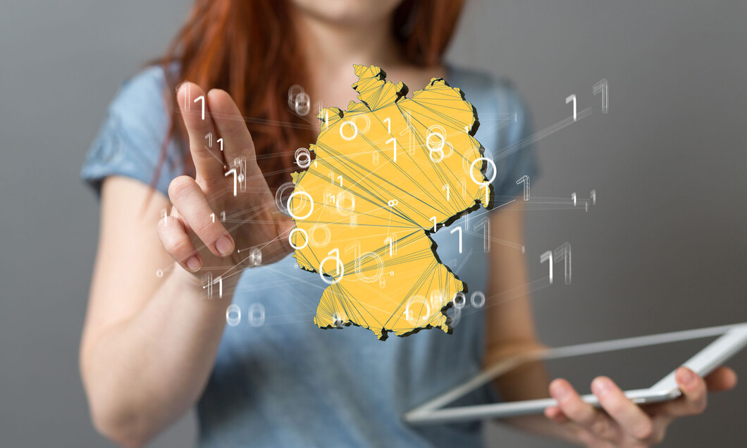 Junge Frau mit einem Tablet in der Hand steht vor einer virtuellen Deutschland-Karte. 