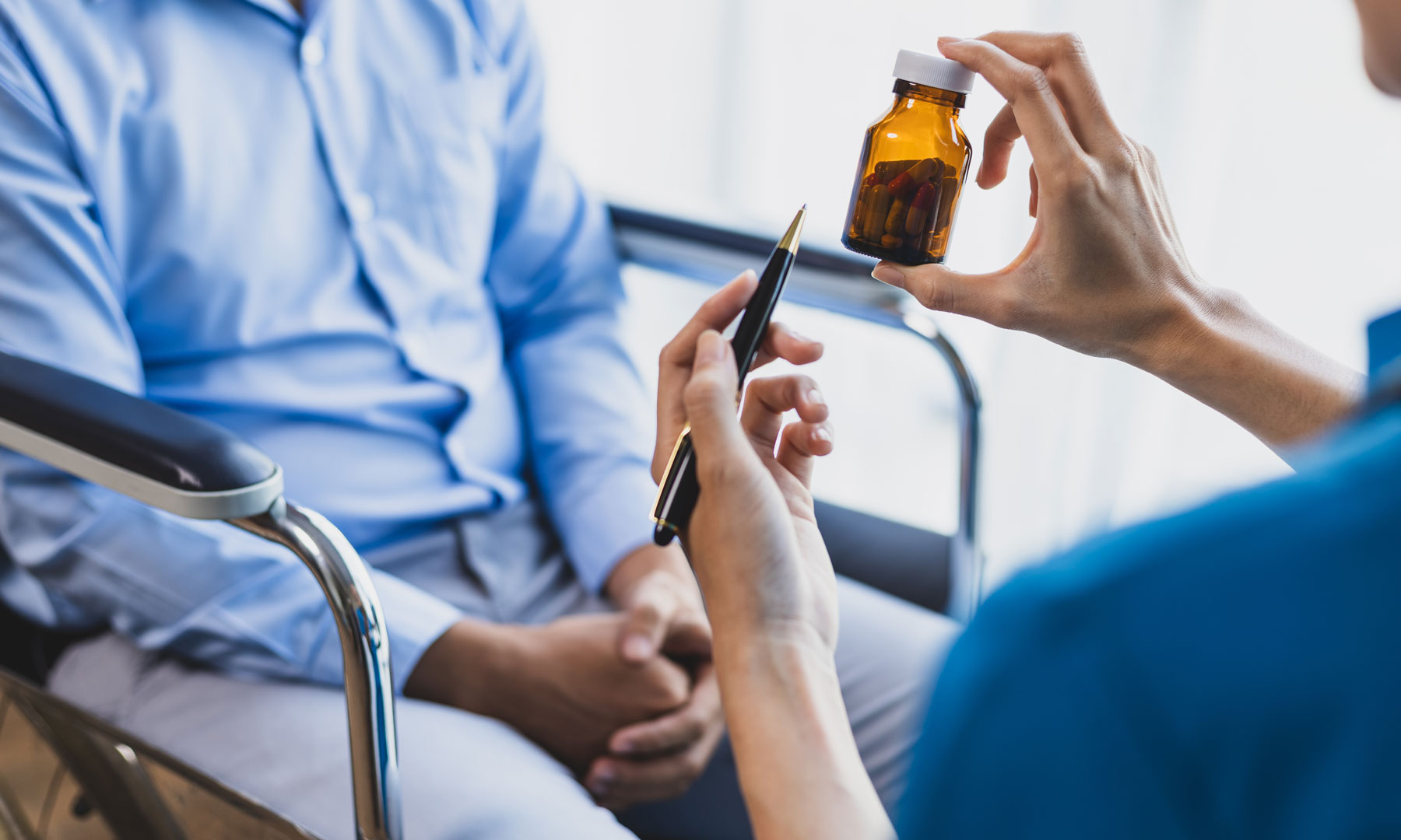 Patient sitzend auf einem Stuhl, daneben eine Ärztin hält eine Pinzette und ein kleines Fläschchen mit Tabletten.